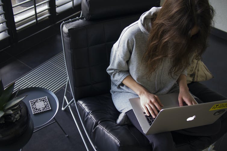 A woman in a hoodie hunches over her laptop.